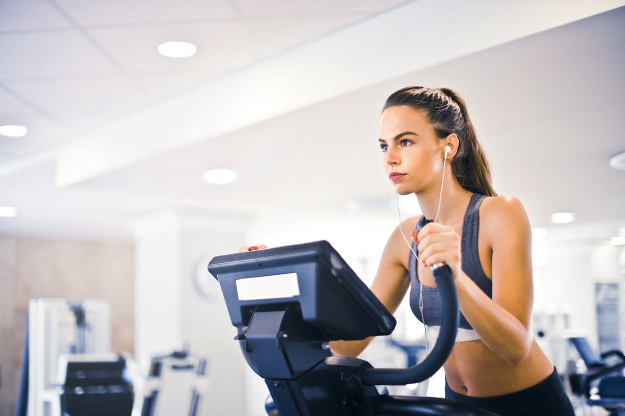 menu-02 Serious fit woman in earphones and activewear listening to music and running on treadmill in light contemporary sports center