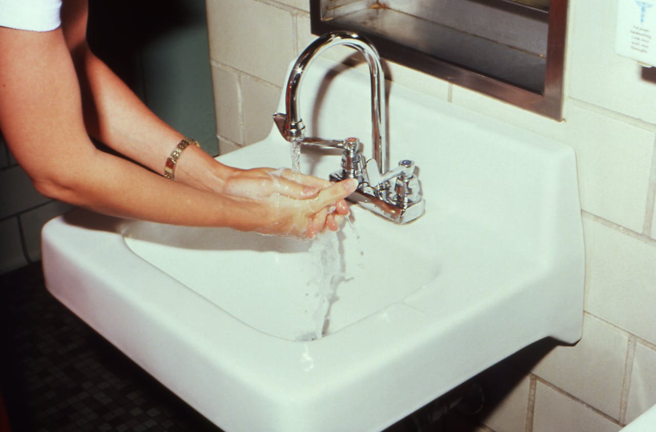 menu-04 A woman washing hands at a bathroom sink, highlighting hygiene and cleanliness.