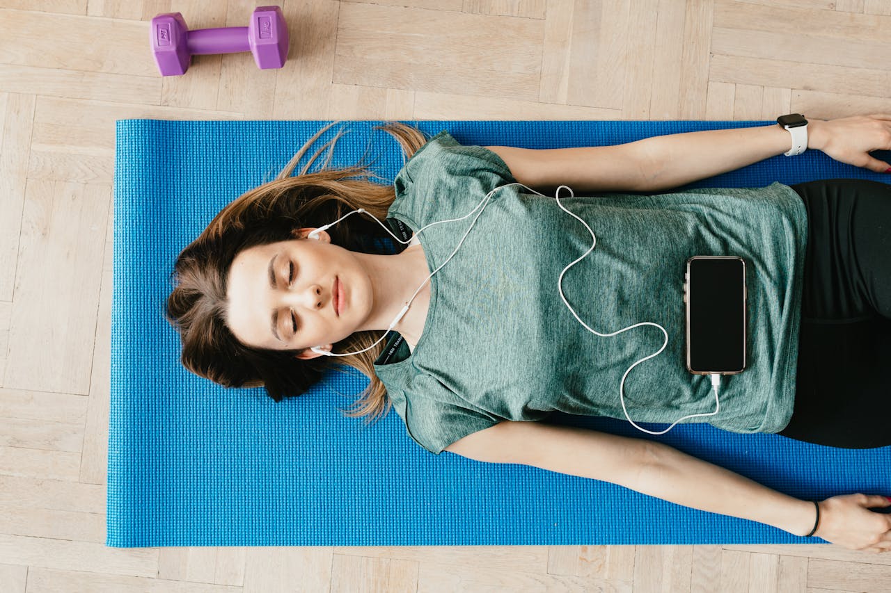 gallery-01 Young woman lying on a yoga mat listening to music for relaxation and mindfulness.