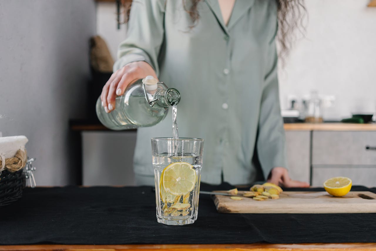 gallery-03 Woman pours water for lemon ginger infusion, promoting health and hydration.