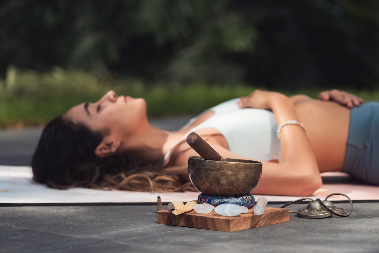 gallery-04 A woman practices relaxation with a singing bowl and crystals in an outdoor setting.
