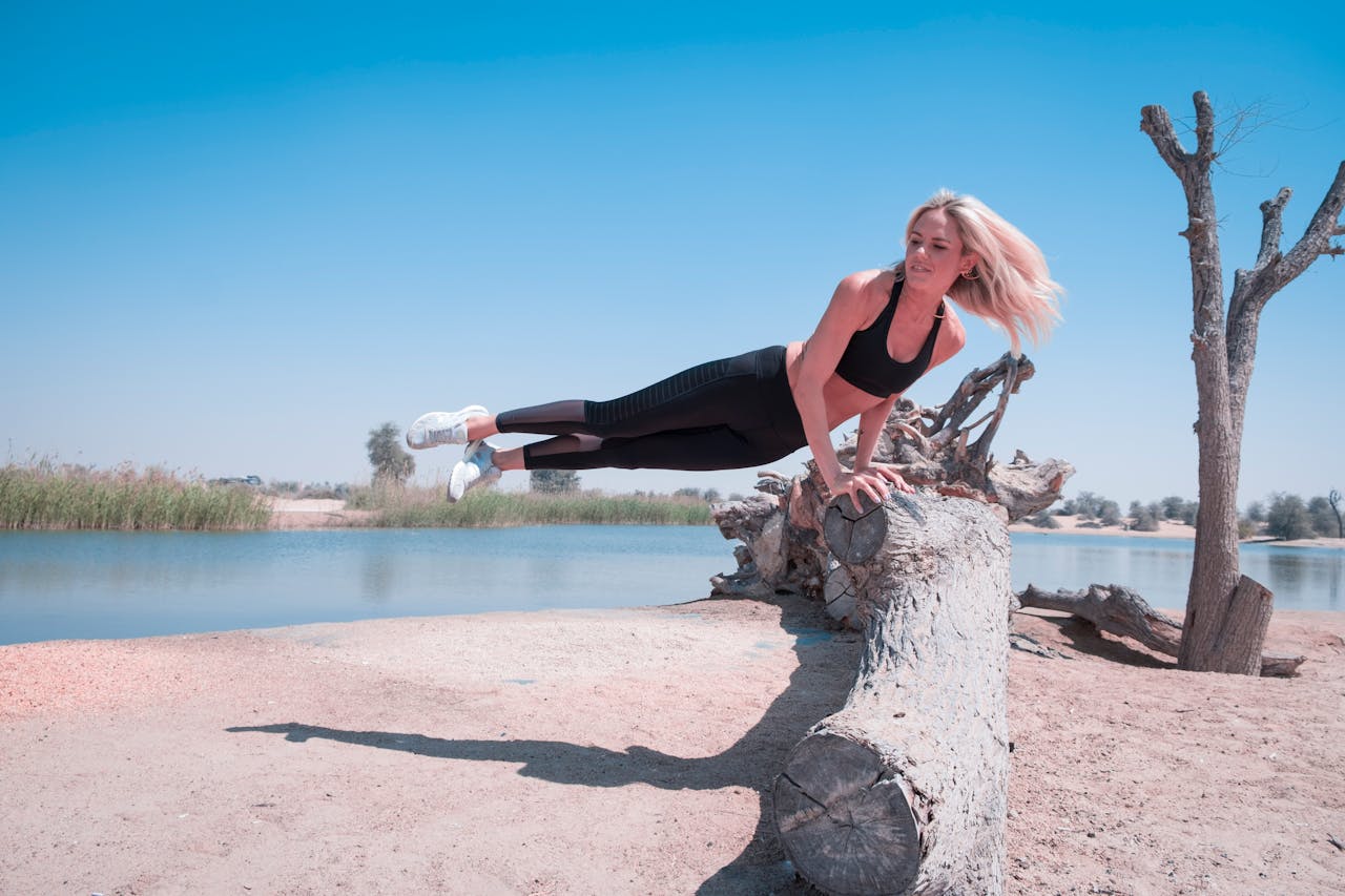 menu-03 Woman performing an athletic pose on a log by a lake in Dubai's desert landscape.